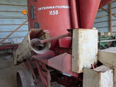 International 1150 grain auger with red hopper and conveyor in storage barn.