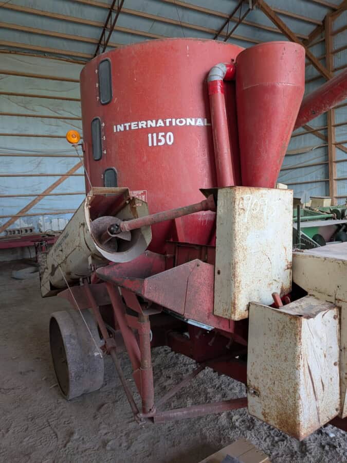 International 1150 grain auger with red hopper and conveyor in storage barn.