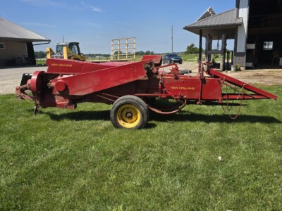 Red New Holland rotary mower with yellow wheels on green grass.