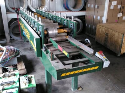 Industrial beaded fascia machine with rollers and control panel in warehouse setting.