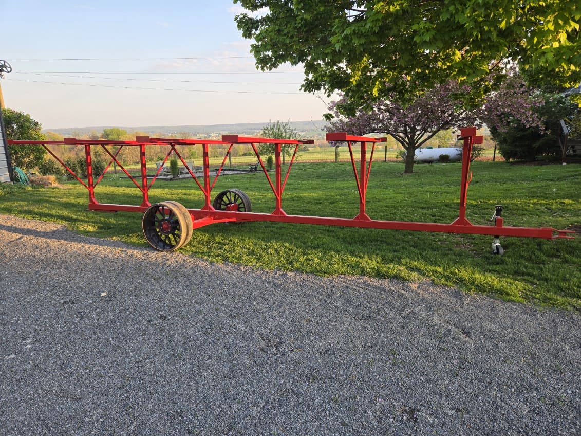 Red tobacco lath trailer with wheels and frame on grassy area under trees.
