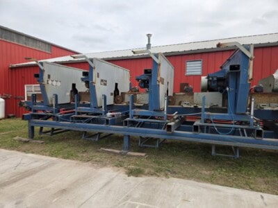 Industrial sawmill equipment with multiple cutting stations on a blue frame.