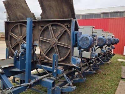 Industrial equipment with large wheels and blue motors, outdoors on grass, under cloudy sky.