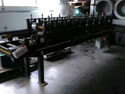 Industrial pipe bending machine in warehouse with metal pipes on shelves.