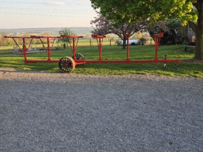 Red tobacco lath trailer with multiple racks and wheels, outdoors near trees and open field.