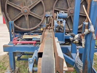 Industrial sawmill equipment with large wheels and cutting blade, blue frame, and hydraulic components.