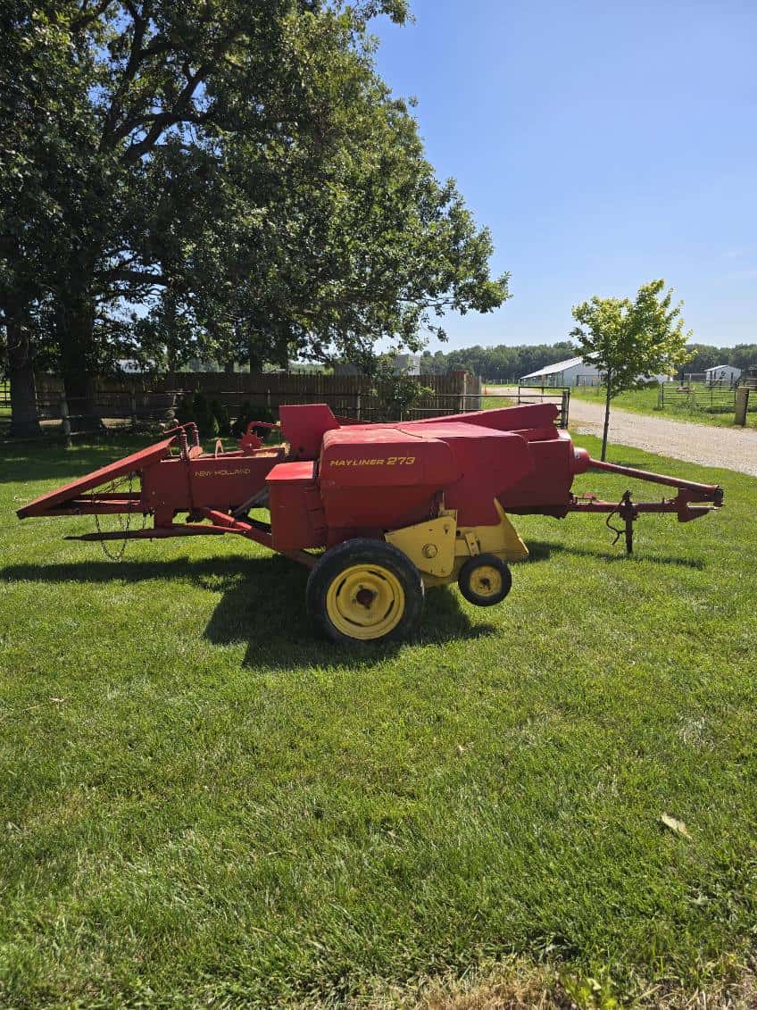 image000003 (19) Red New Holland 273 hay baler with yellow wheels on green grass under blue sky.