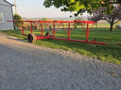 Red tobacco lath trailer with wheels parked on gravel near a tree and building.
