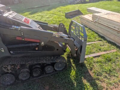 Compact tracked loader with front attachment on grassy construction site.