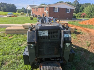 Compact construction equipment with diesel engine on a grassy area near a brick house.