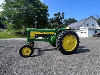 John Deere 5300 tractor with green body and yellow wheels on gravel surface under blue sky.