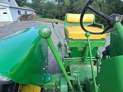Green John Deere 2020 tractor with yellow seat and front loader attachment on gravel driveway.