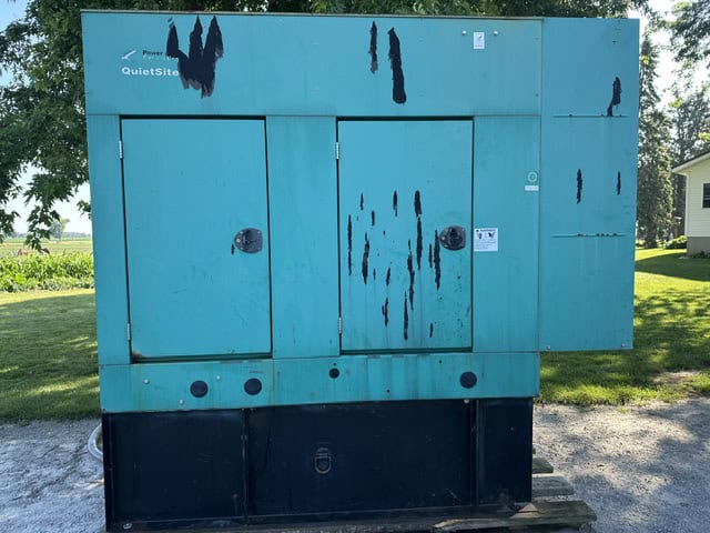 Blue industrial generator with visible rust and wear, outdoors on a concrete pad.