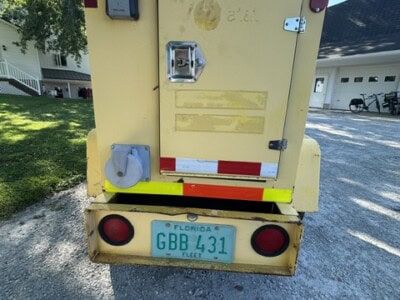 Yellow utility trailer with Florida license GBB 431 and rear lights, parked on gravel driveway.