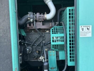 CUMMINS ONAN 50 kW generator engine with visible exhaust pipe and control panel inside teal enclosure.