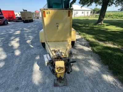 Yellow portable generator with green top and towing hitch on gravel surface.