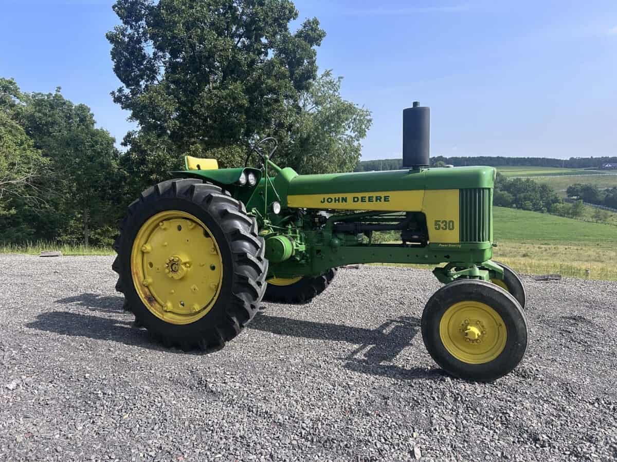 John Deere 530 vintage tractor with green body and yellow wheels on gravel surface.