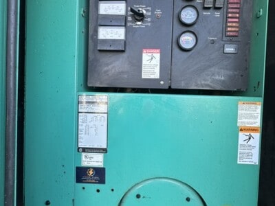 Industrial generator control panel with gauges and switches in a green metal enclosure.