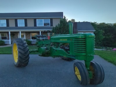 John Deere Model A vintage tractor with large rear tires and smaller front tires, parked on a driveway.