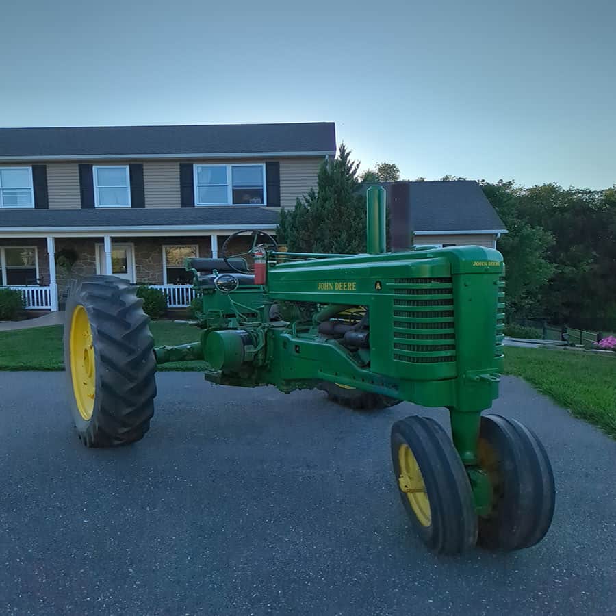 Green vintage John Deere tractor with yellow wheels parked on driveway near house.