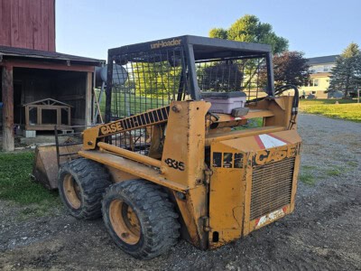Yellow CASE 1835 skid steer loader with protective cage and large tires on gravel surface.