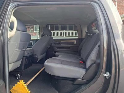 Interior of a black pickup truck showing rear seats and cleaning tool on floor.