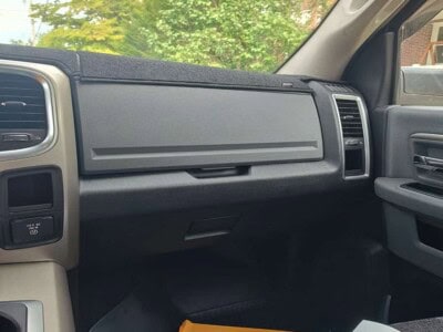 View of the vehicle's dashboard with a closed glove compartment and some items in the passenger footwell.