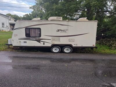 2014 Rockwood Roo 19 camper trailer with beige exterior and black accents, parked on a street with trees in the background.