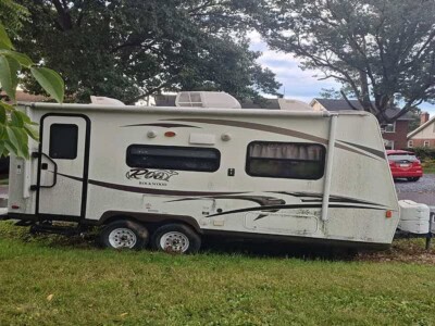 2014 Rockwood Roo 19 camper trailer with visible wear and dirt, parked on grass under trees.