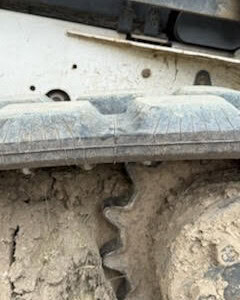 Close-up of excavator track and sprocket with dirt and mud.