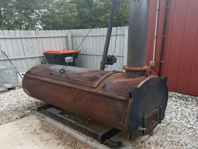 Rusty industrial incinerator with a vertical chimney and metal door, placed outdoors on concrete base.