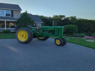 Green John Deere tractor with yellow wheels parked on driveway in front of house.