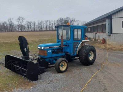 Blue Ford 2120 tractor with front blade attachment on a farm.
