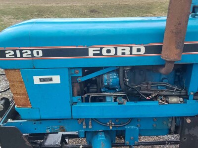 Blue Ford 2120 tractor with visible engine and controls in an outdoor setting.