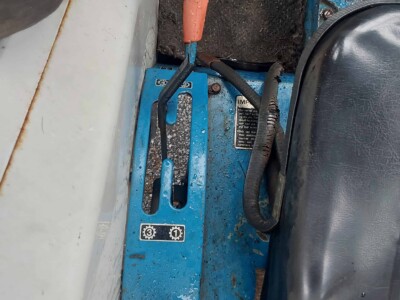 Blue control lever with orange handle on a tractor floor, showing wear and dirt.