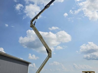 2015 JLG X700AJ boom lift with extended arm and basket against blue sky with clouds.
