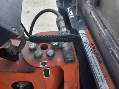 Close-up of hydraulic hoses and components on orange construction machinery.