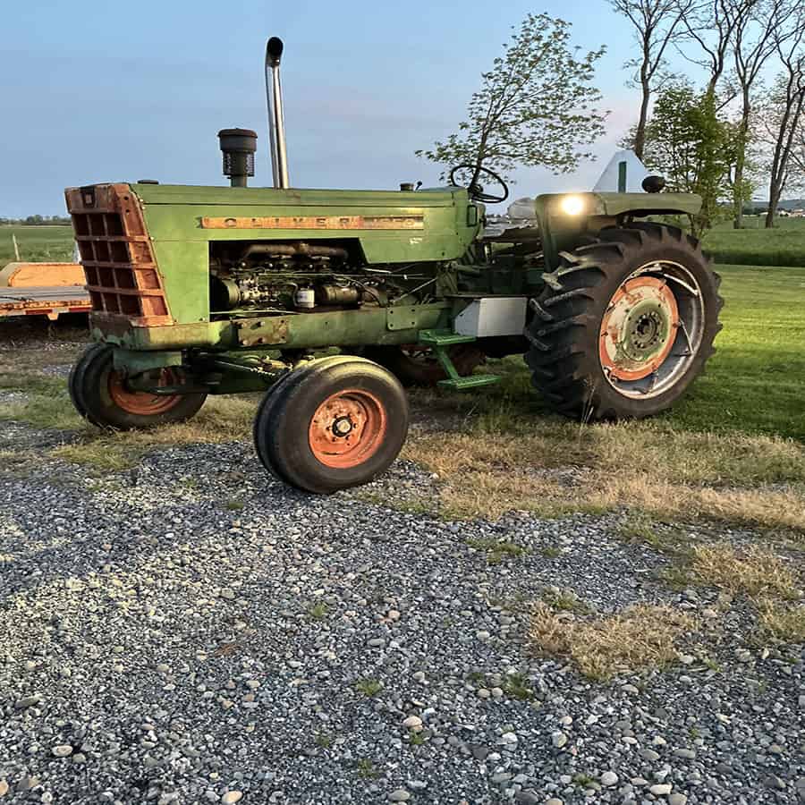 Green Oliver 1550 tractor with front loader and large rear tires on grassy field.