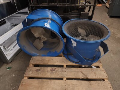 Two blue portable industrial fans with protective mesh covers on a wooden pallet.
