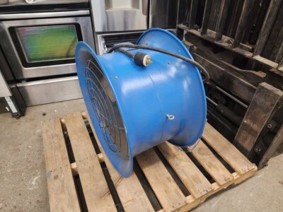 Blue industrial blower fan with protective grille on a wooden pallet.