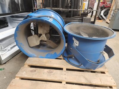 Blue industrial fan and blower with large circular intake and mesh outlet on wooden pallet.