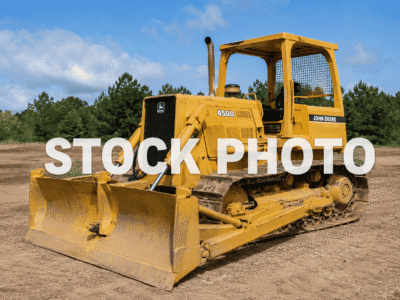 John Deere 450D crawler dozer with blade and tracks on dirt under blue sky.
