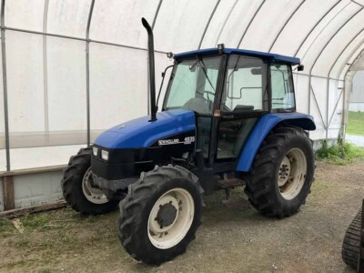 New Holland 4835 tractor with enclosed cab and large rear tires in greenhouse setting.