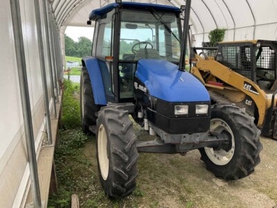 Blue New Holland tractor with enclosed cab and large tires in a storage shed.