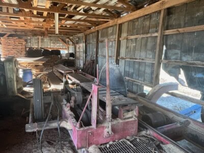 Old sawmill machinery with rust and wear in rustic barn setting.