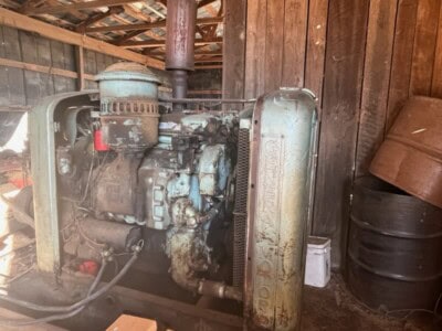 Old John Deere diesel engine with visible wear and rust in a wooden shed.