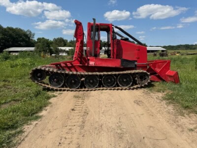Red KMC 1000AG track skidder with cab and blade on grassy field under blue sky.
