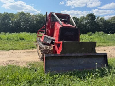KMC 1000AG track skidder with blade attachment on grassy field under blue sky.