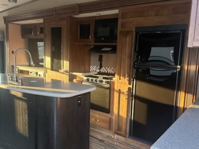 Contemporary kitchen featuring black refrigerator, wooden cabinets, and island with sink and faucet.