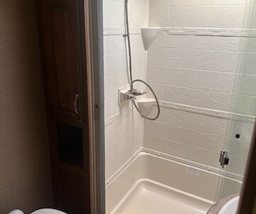 Compact shower stall with white tiled walls, glass door, and showerhead, in a bathroom corner.